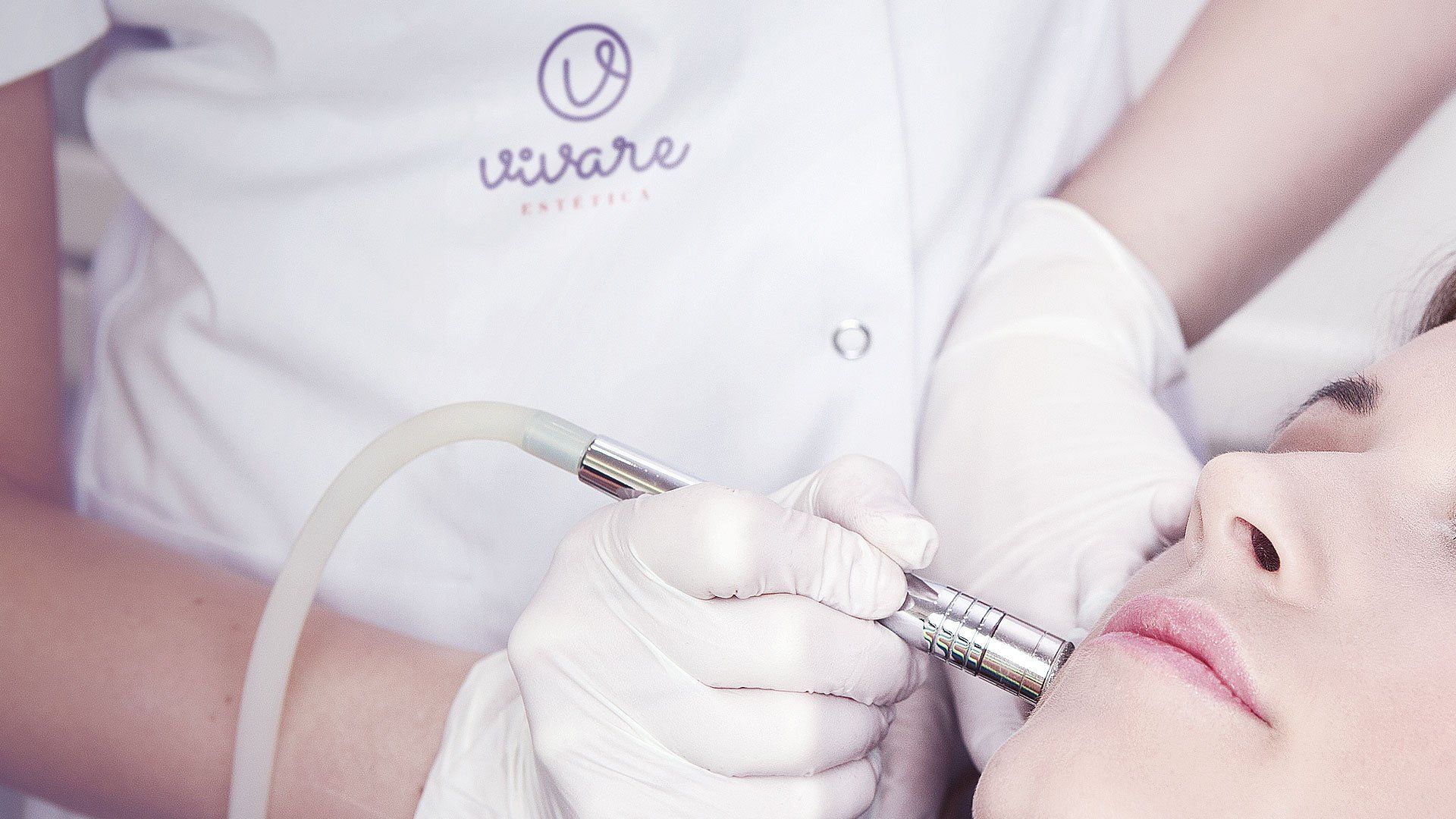 Esteticista realizando um tratamento de pele no rosto de uma pessoa. A pessoa está deitada e o profissional utiliza um instrumento manual.