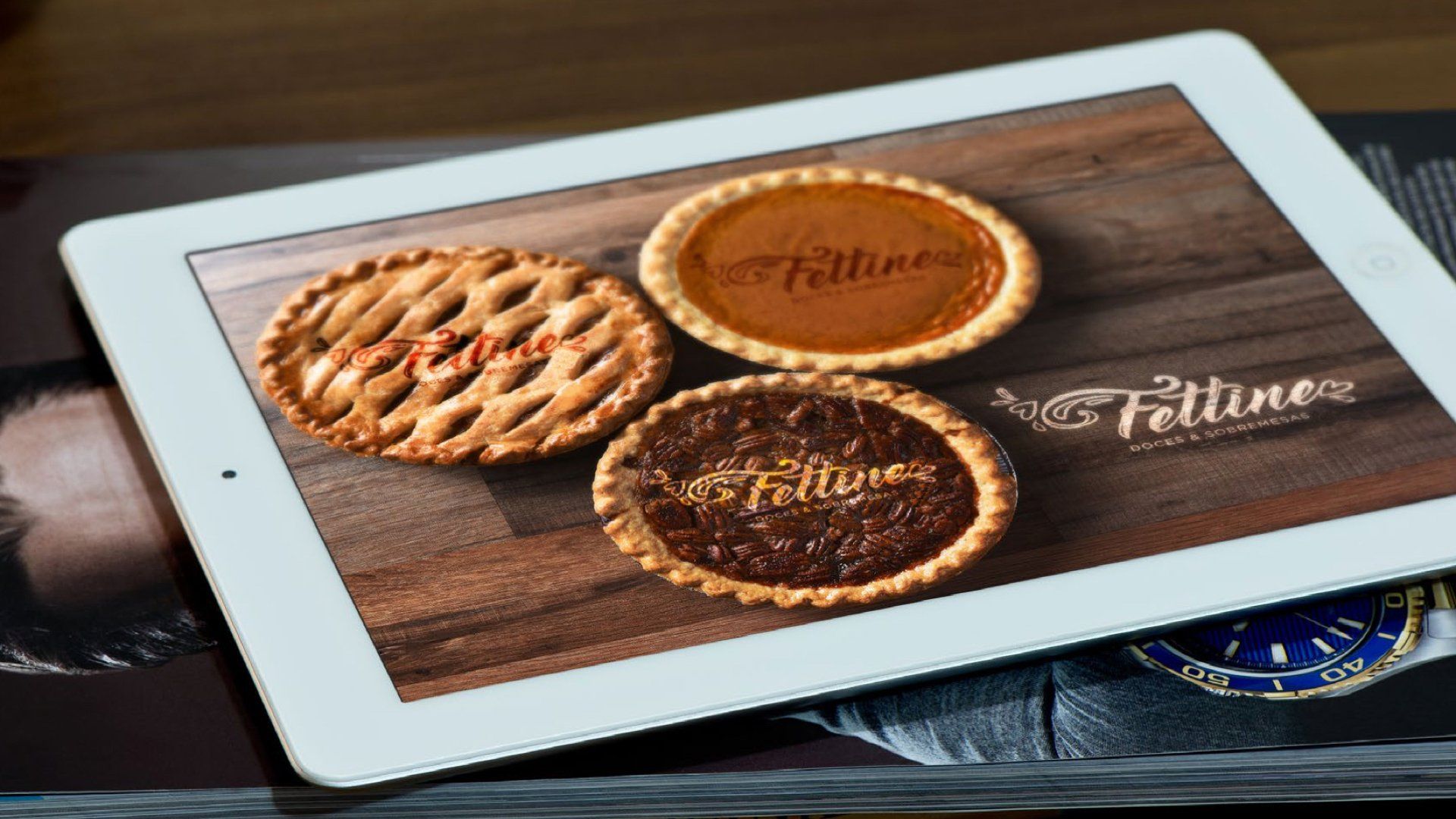 Um tablet com três tortas na tela está sobre uma mesa.