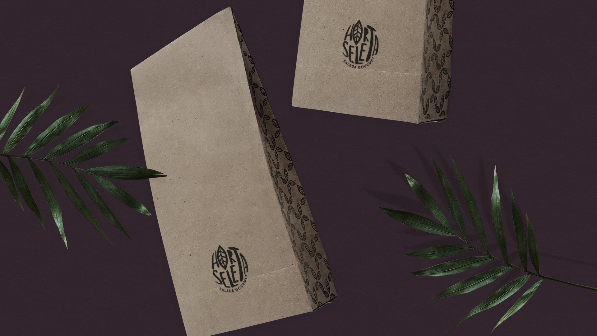 Dois sacos de papel pardo com um logotipo circular, folhas verde-escuras sobre um fundo roxo escuro.