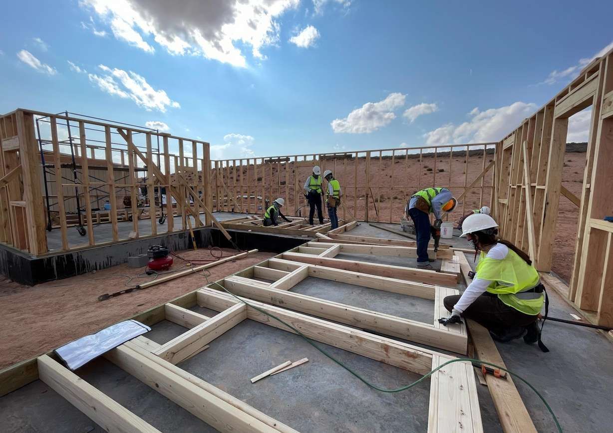 Construction site with workers framing a building; bright sky overhead.