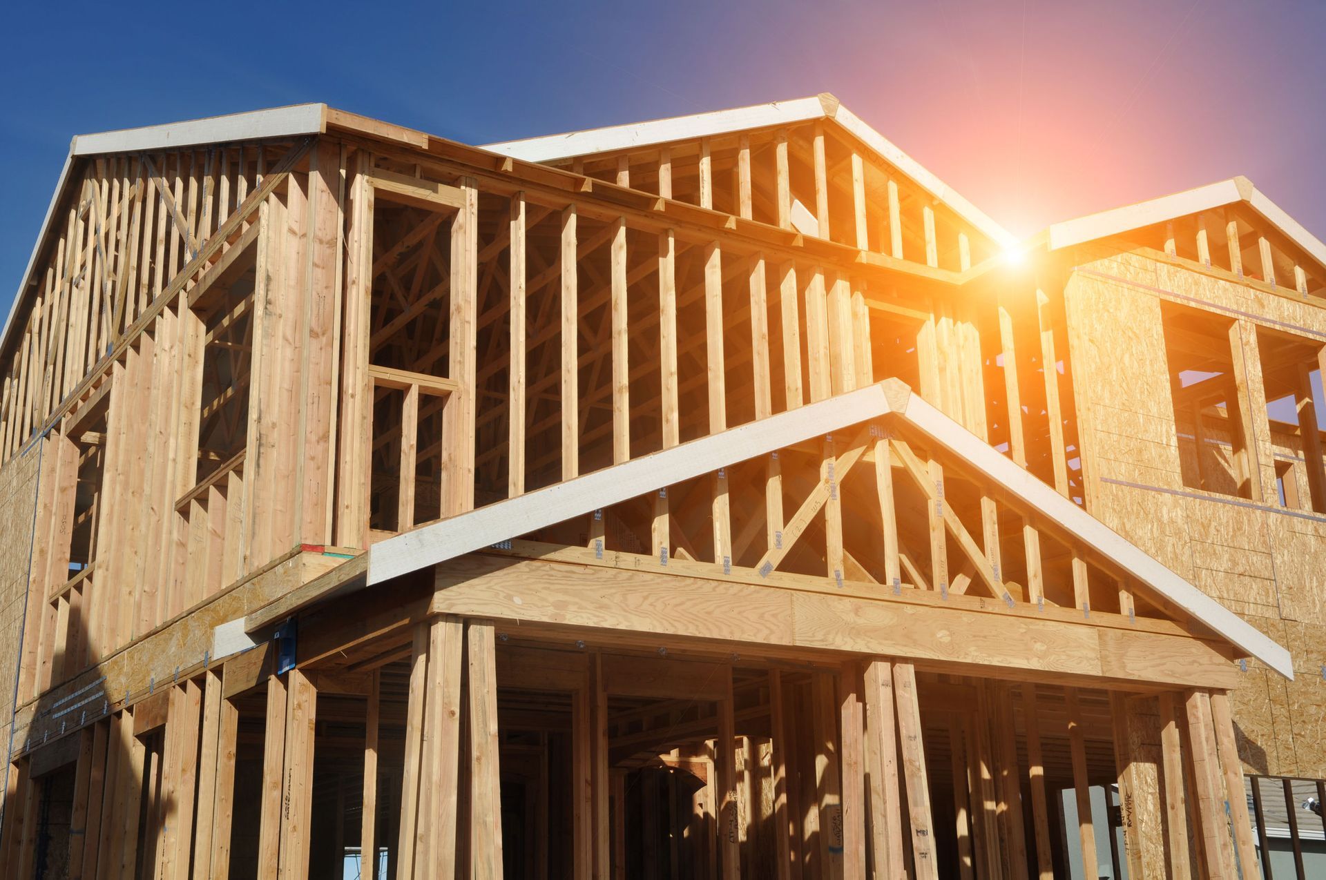 Wooden framework of a two-story house under construction, illuminated by sunlight.