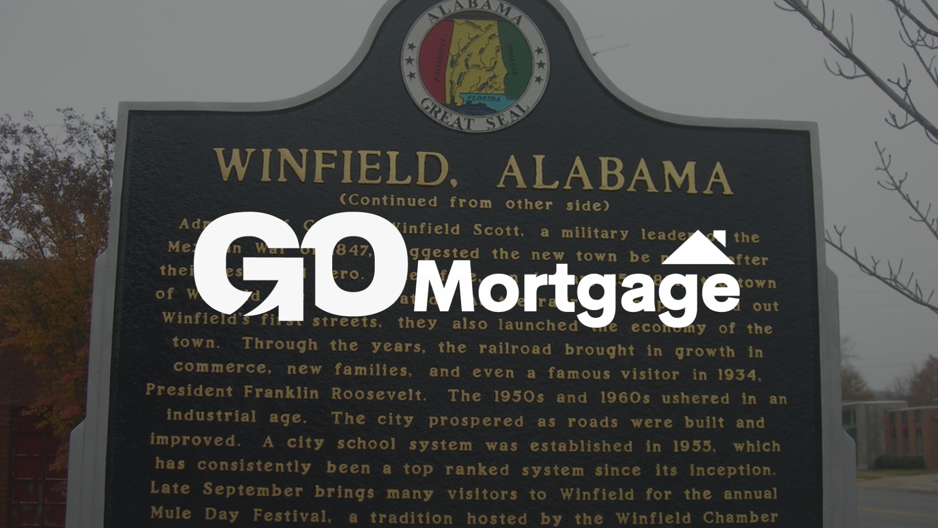 Historical marker in Winfield, Alabama, partially obscured by a 