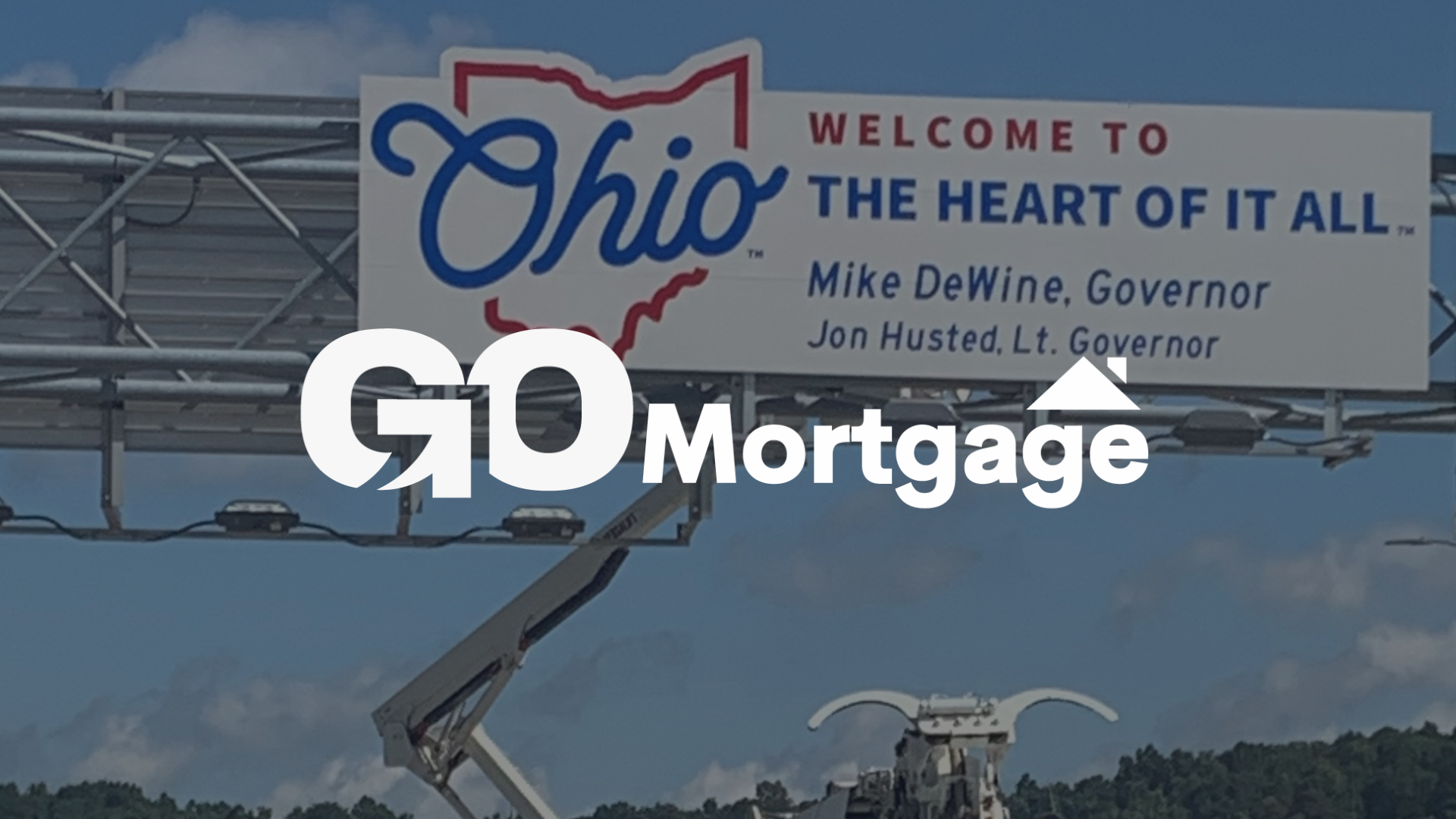 A billboard that says welcome to ohio the heart of it all with the gomortgage logo in the foreground