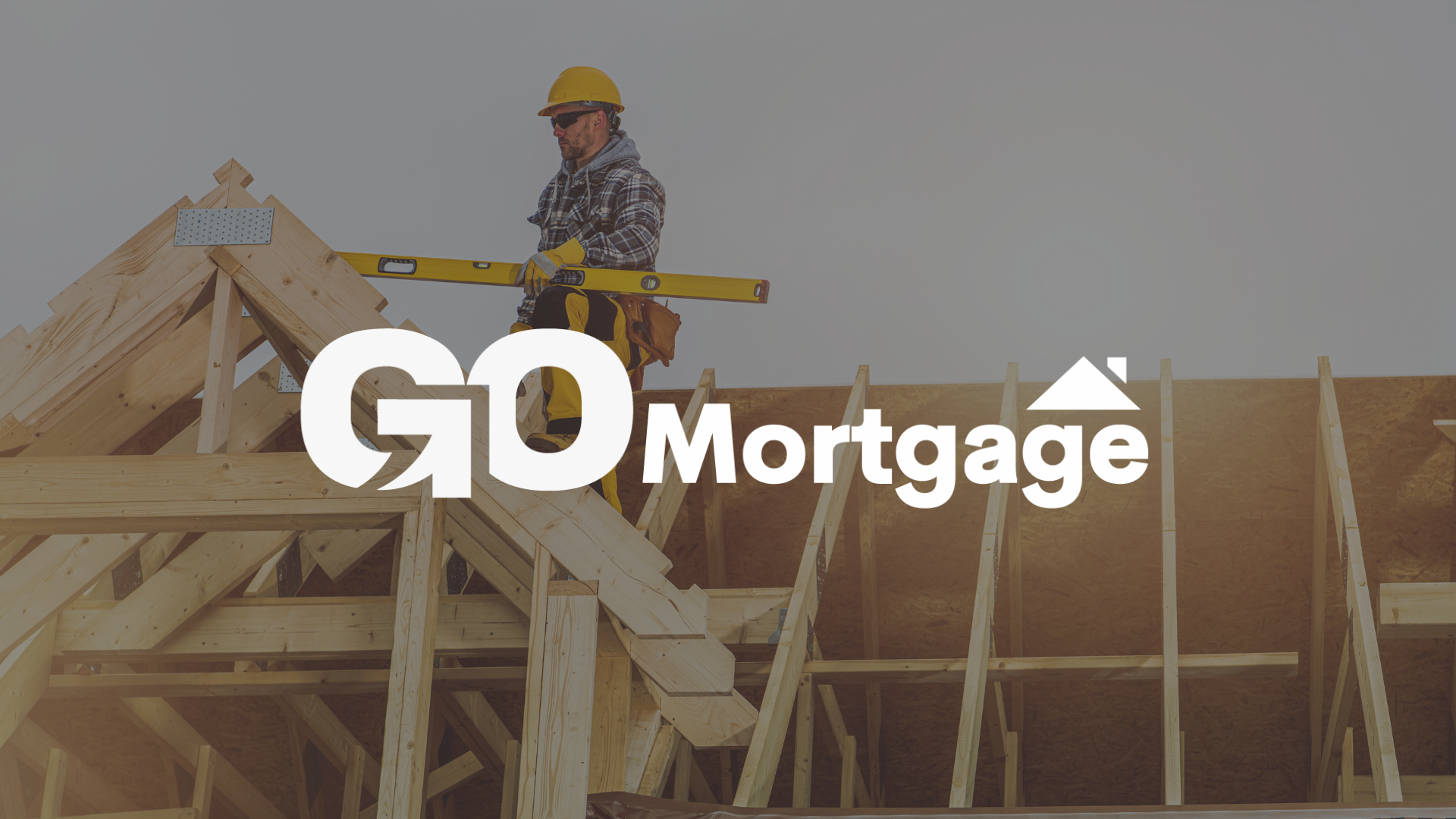 A man is standing on top of a wooden structure holding a level with go mortgage logo on top