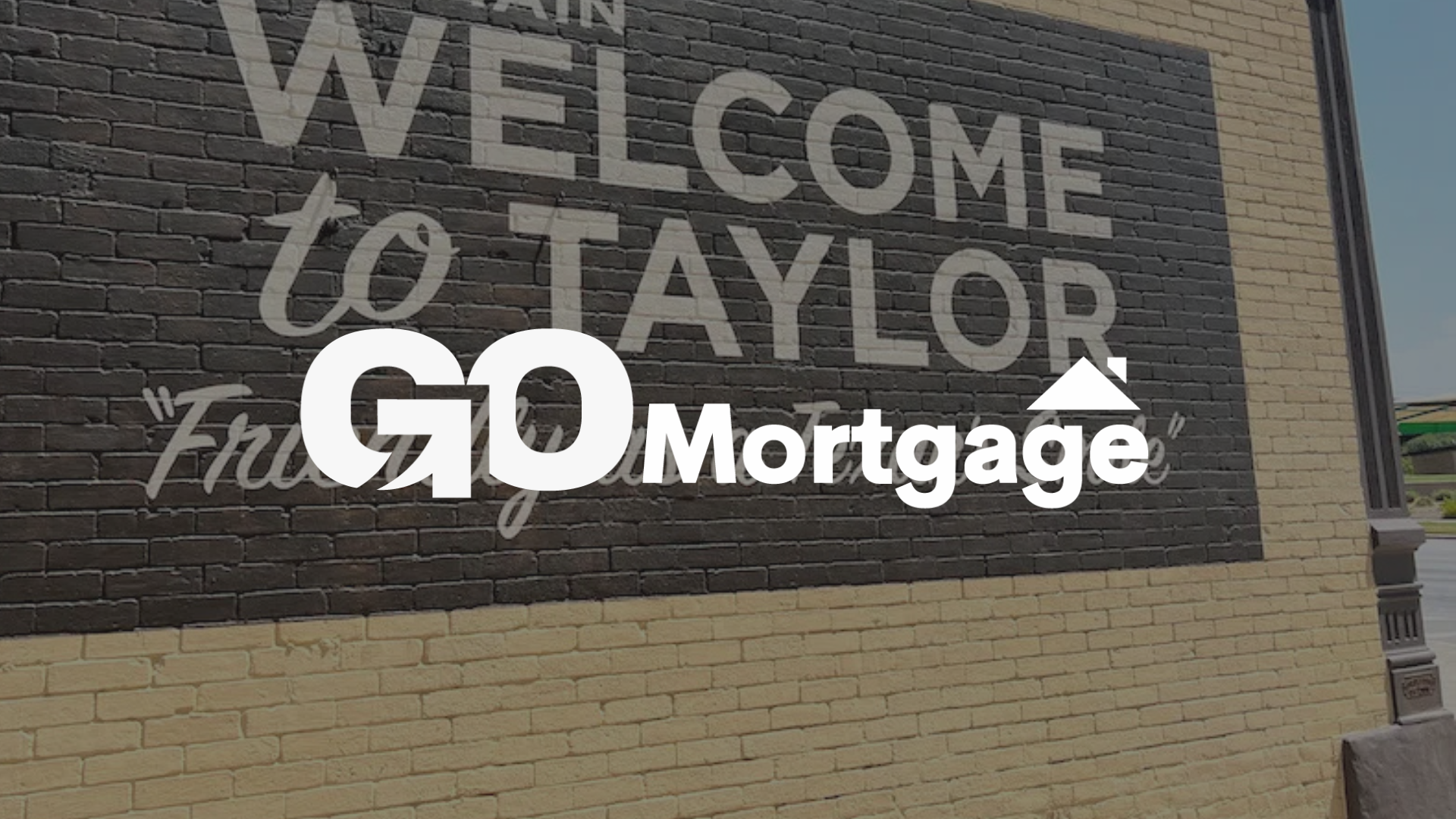 Sign: Welcome to Taylor, TX; GO Mortgage logo on a brick wall.