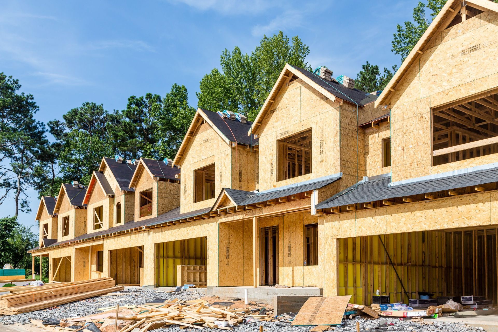 Row of townhouses under construction; wooden frames with black roofing against a blue sky.