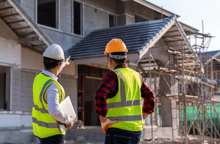 Two construction workers are standing in front of a house under construction.