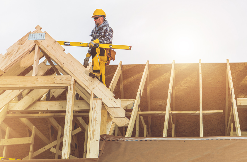 A construction worker is working on the roof of a house under construction.