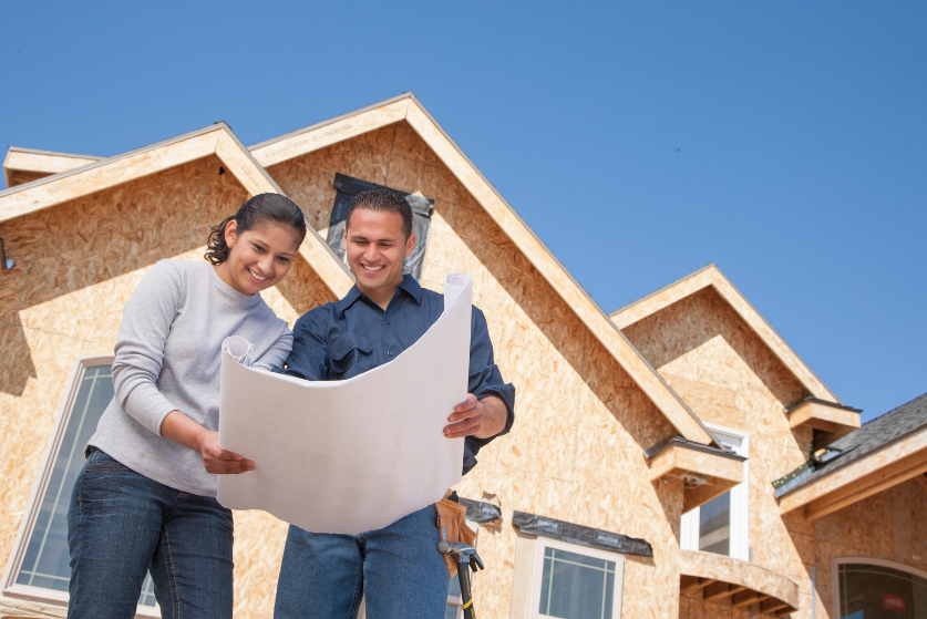 A man and a woman are looking at blueprints in front of a house under construction.