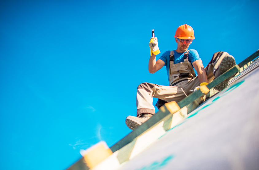 A man is sitting on top of a roof holding a bottle of beer.