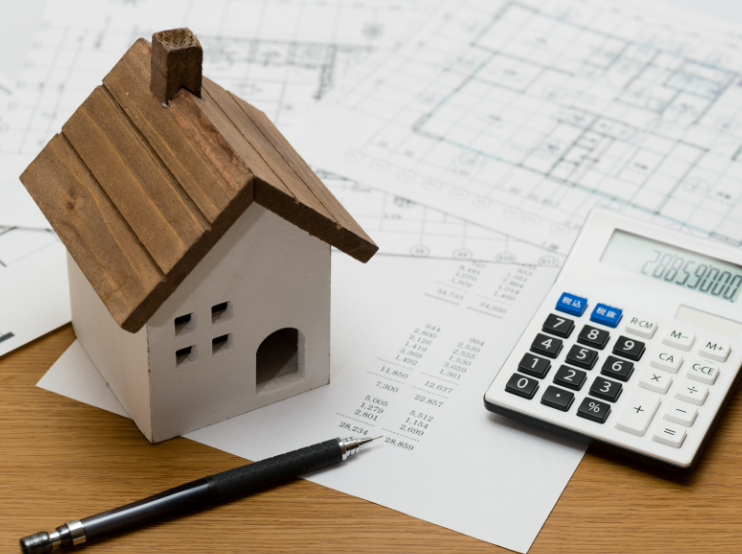 A model house is sitting next to a calculator and a pen on a table.