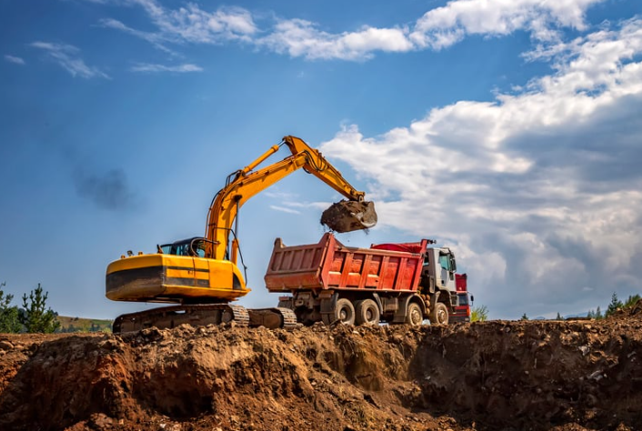 A yellow excavator is loading dirt into a red dump truck.