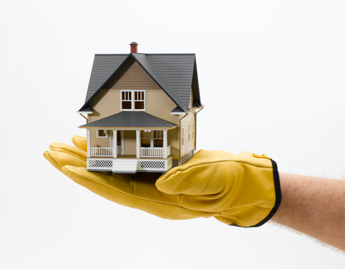 A person wearing yellow gloves is holding a model house