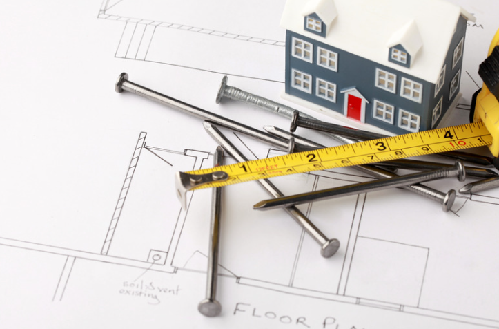 A model house is sitting on top of a floor plan next to nails and a tape measure.