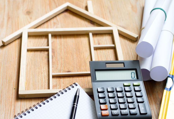 A calculator sits on a wooden table next to a model house