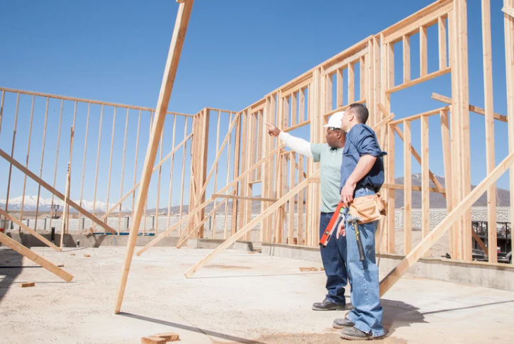 Two construction workers are standing in front of a building under construction.