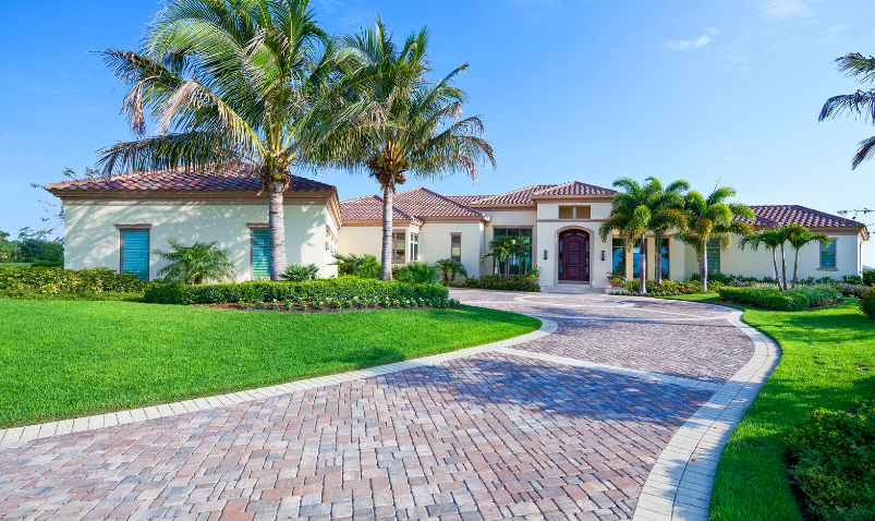 A large white house with a brick driveway and palm trees in front of it.