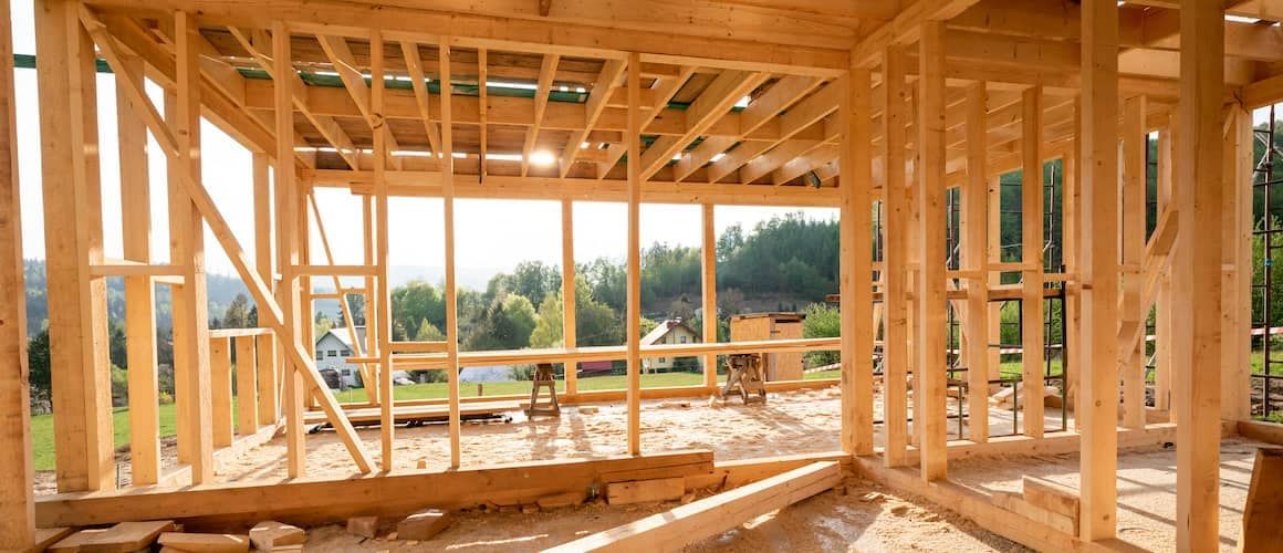 Wooden frame of a house under construction; a sunny landscape can be seen through the window openings.