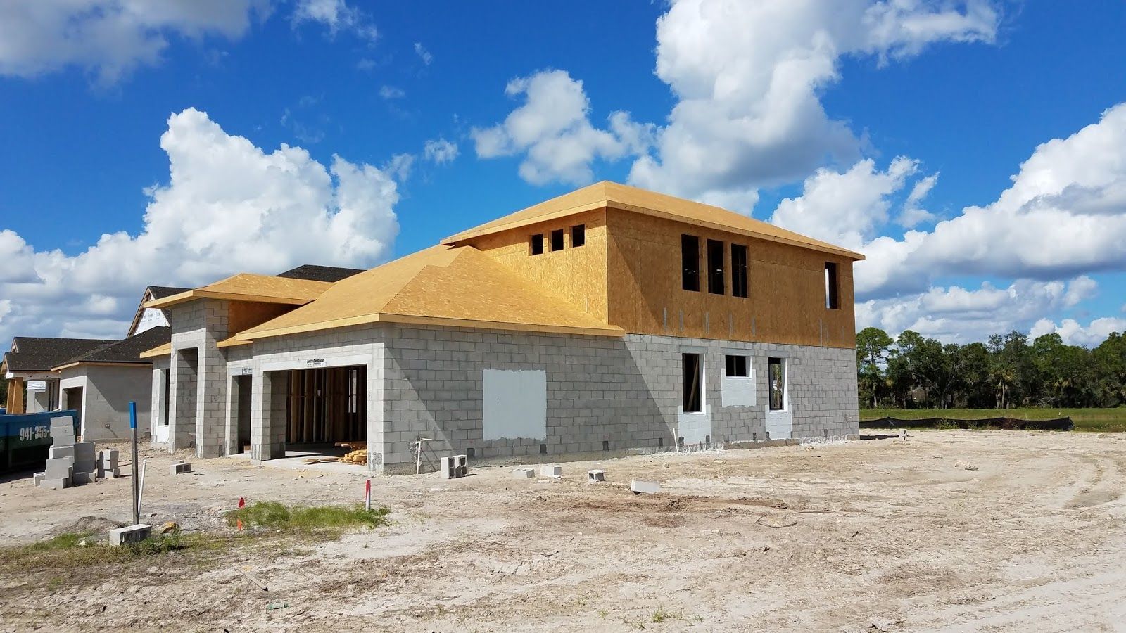 House under construction with concrete block walls, wooden roof frame, and blue sky.