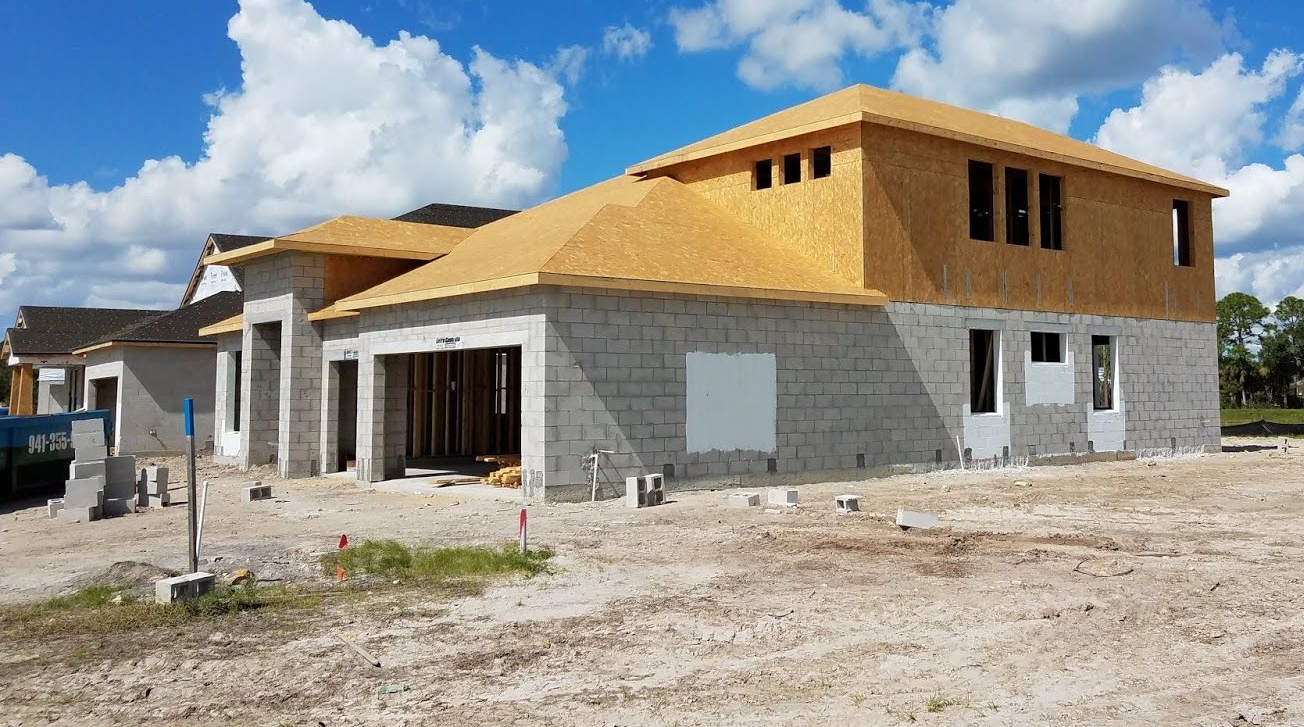 New house under construction with cement block walls and unfinished roof against a blue sky.