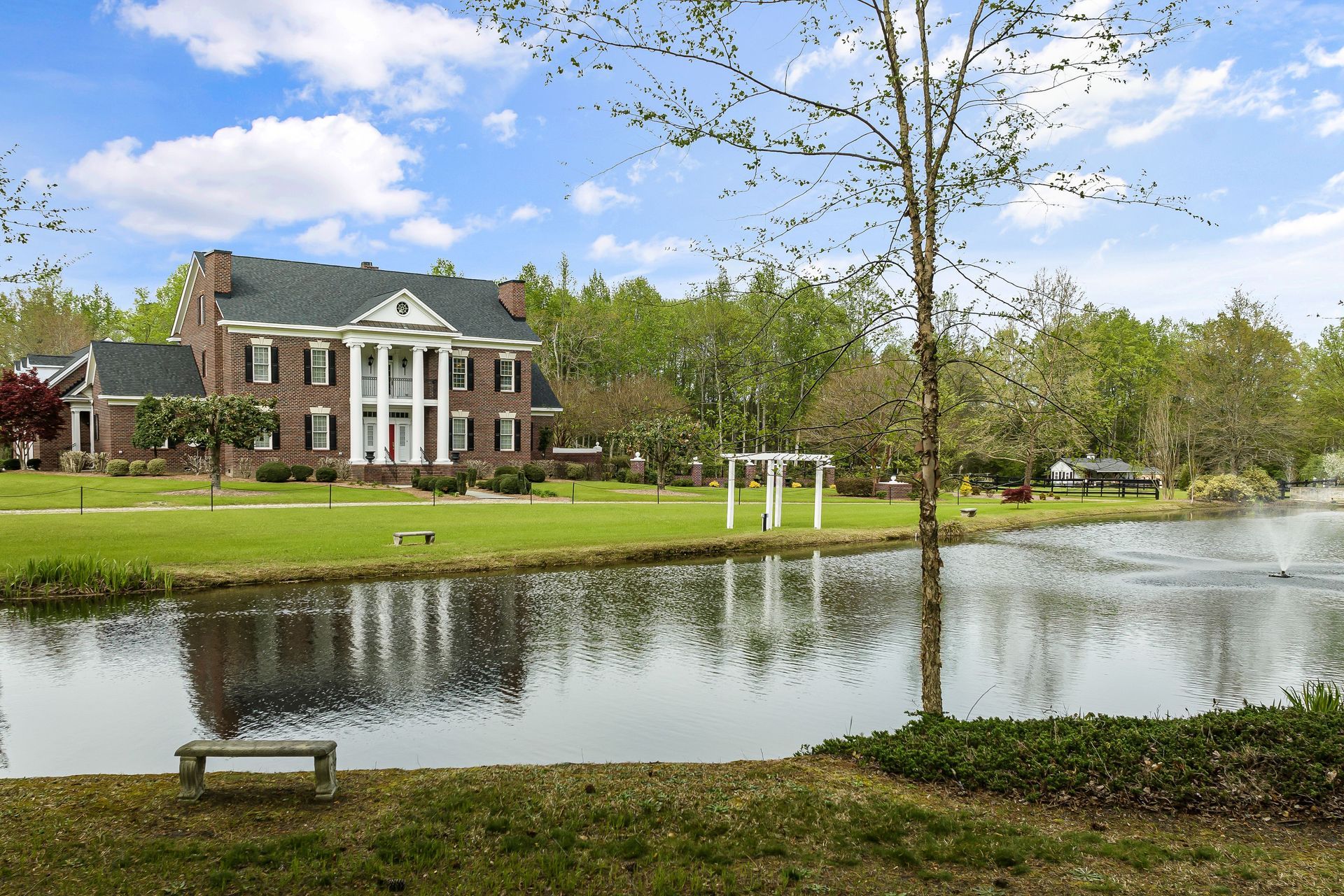 Brick house beside a pond with spring trees and a blue sky