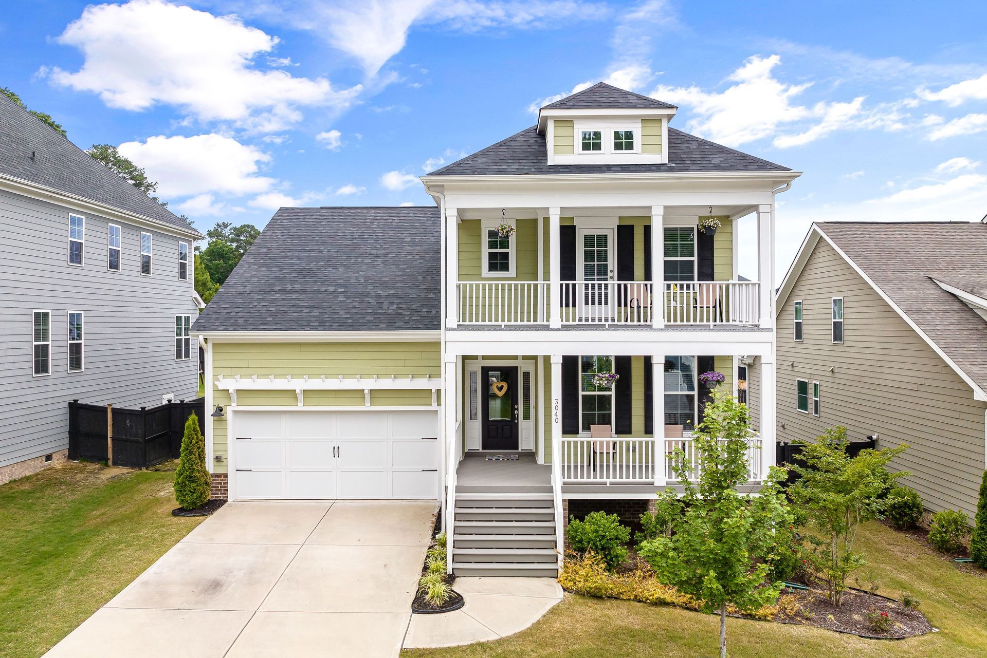 Two-story white house with front porch, garage, and steps, on a sunny suburban street.