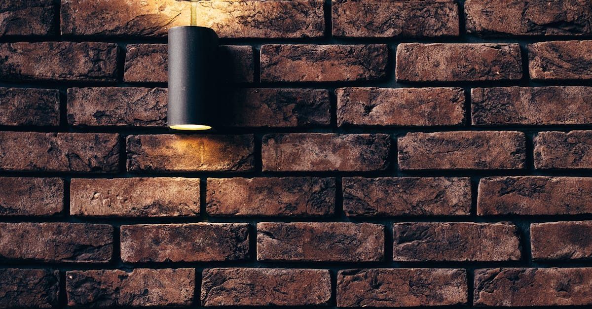 Black outdoor light fixture on a rustic brown brick wall, casting warm light downward.