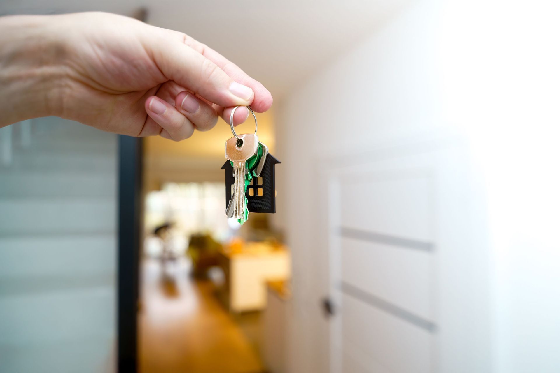 Hand holding a set of house keys in front of a blurred apartment hallway doorway