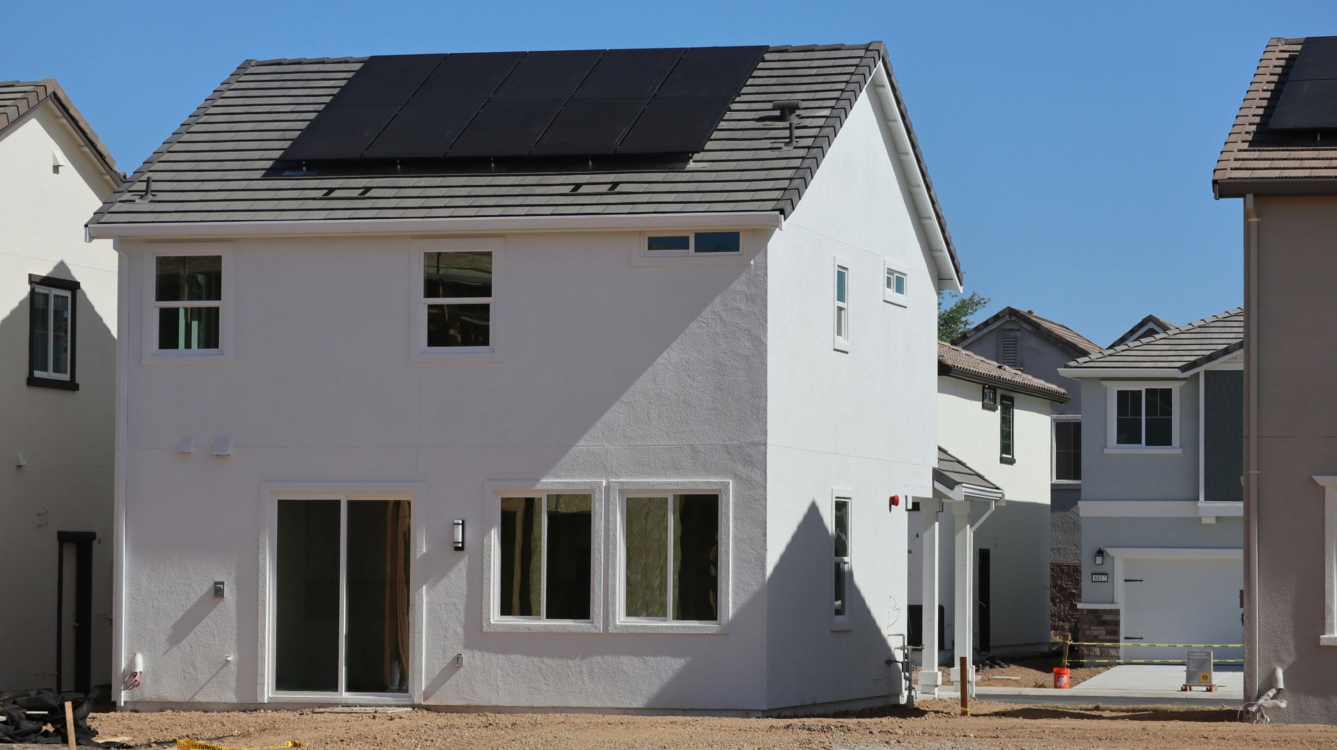 New white houses under construction in a residential neighborhood, with dark roof panels visible.