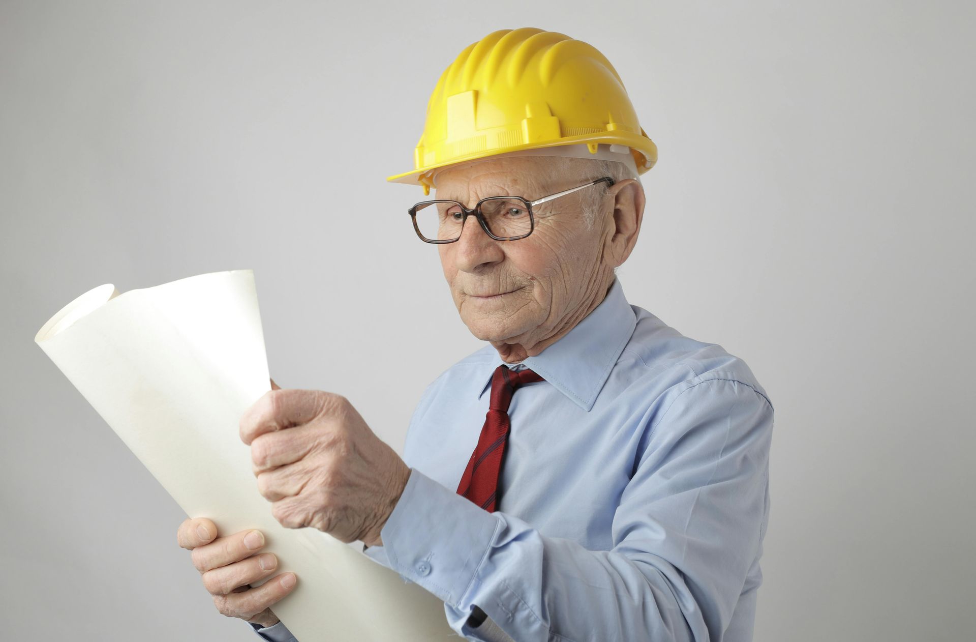 An older man wearing a hard hat and glasses is looking at a blueprint.