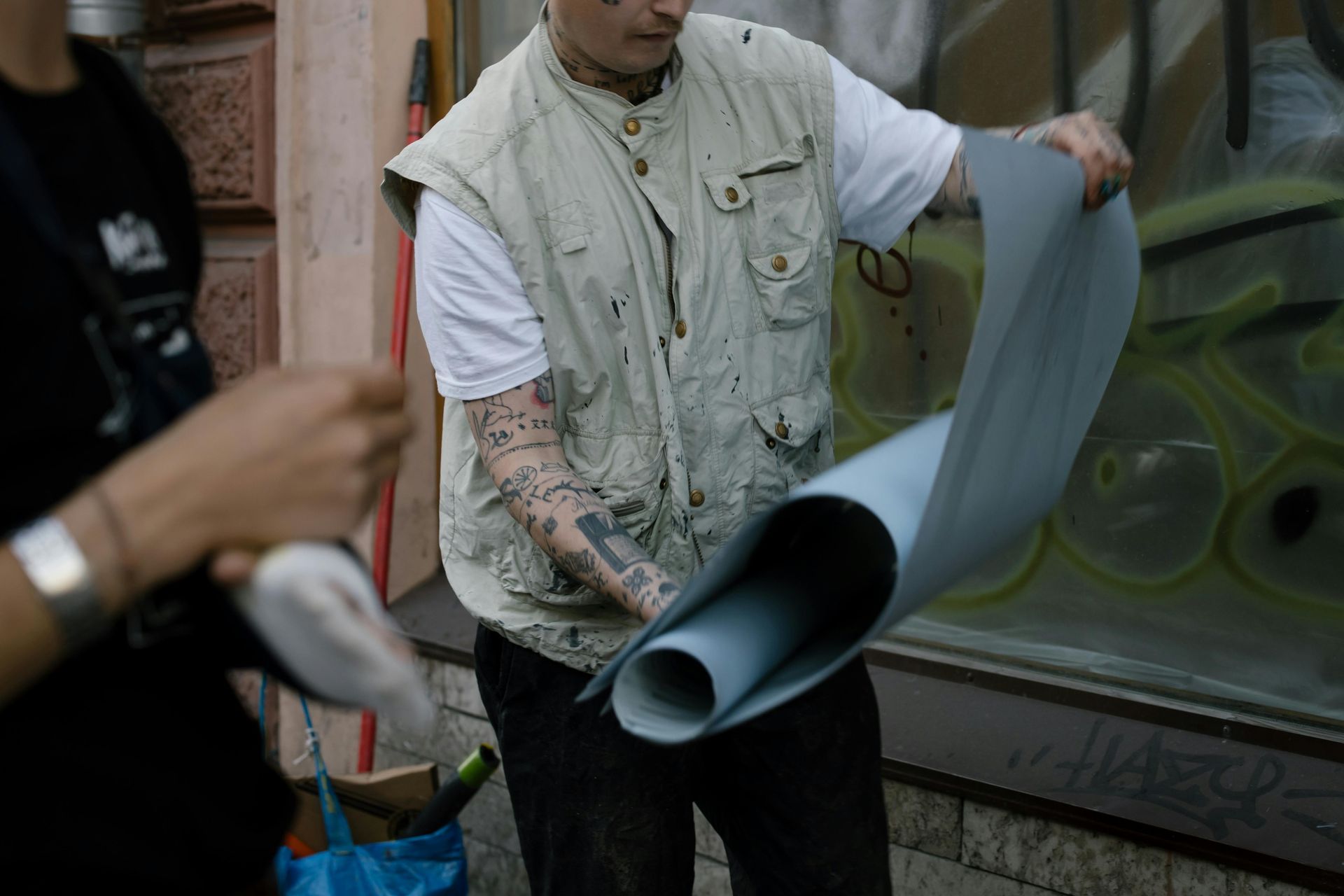 A man with tattoos on his arm is holding a roll of paper.