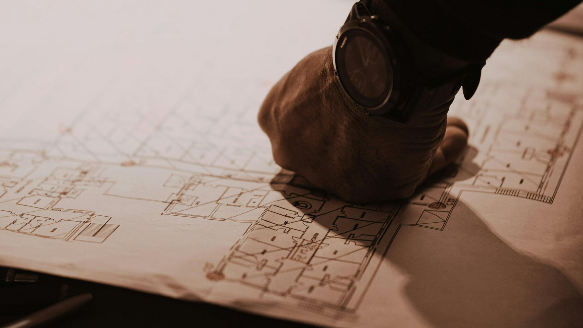 Wood-framed house under construction with exposed plywood, orange safety netting, and a red dumpster in front