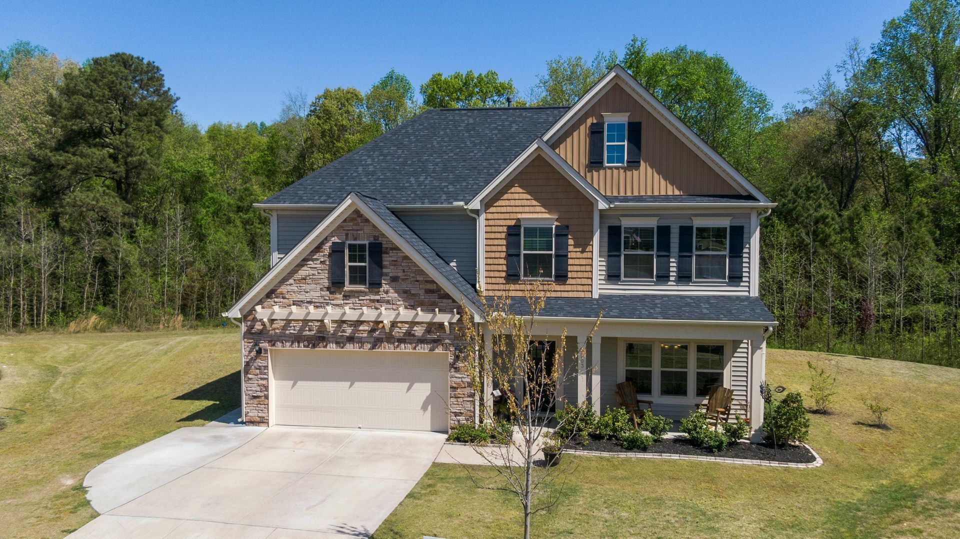 Two-story suburban house with gray siding, stone accents, front porch, and a two-car garage under a clear blue sky