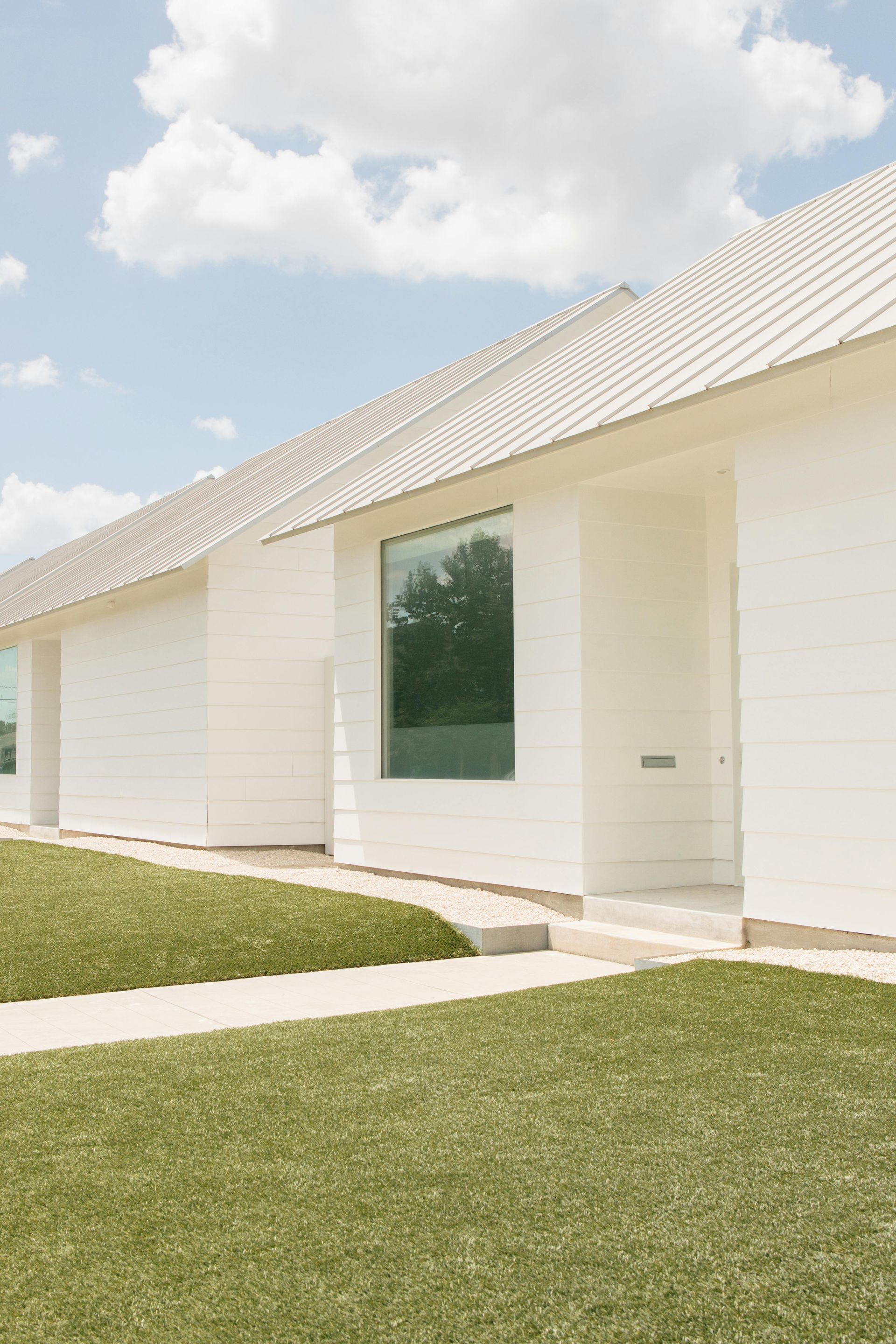 White house with a green lawn and a large window reflecting trees under a blue sky.