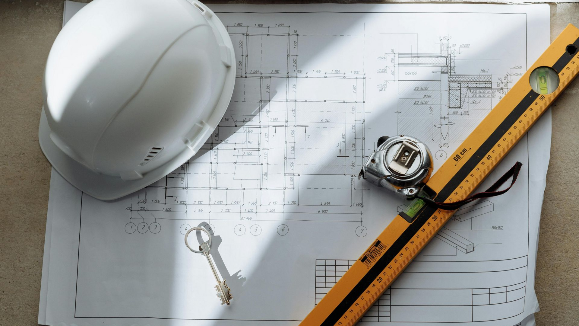 Hard hat, tape measure, and key on blueprints with a yellow level, suggesting construction planning