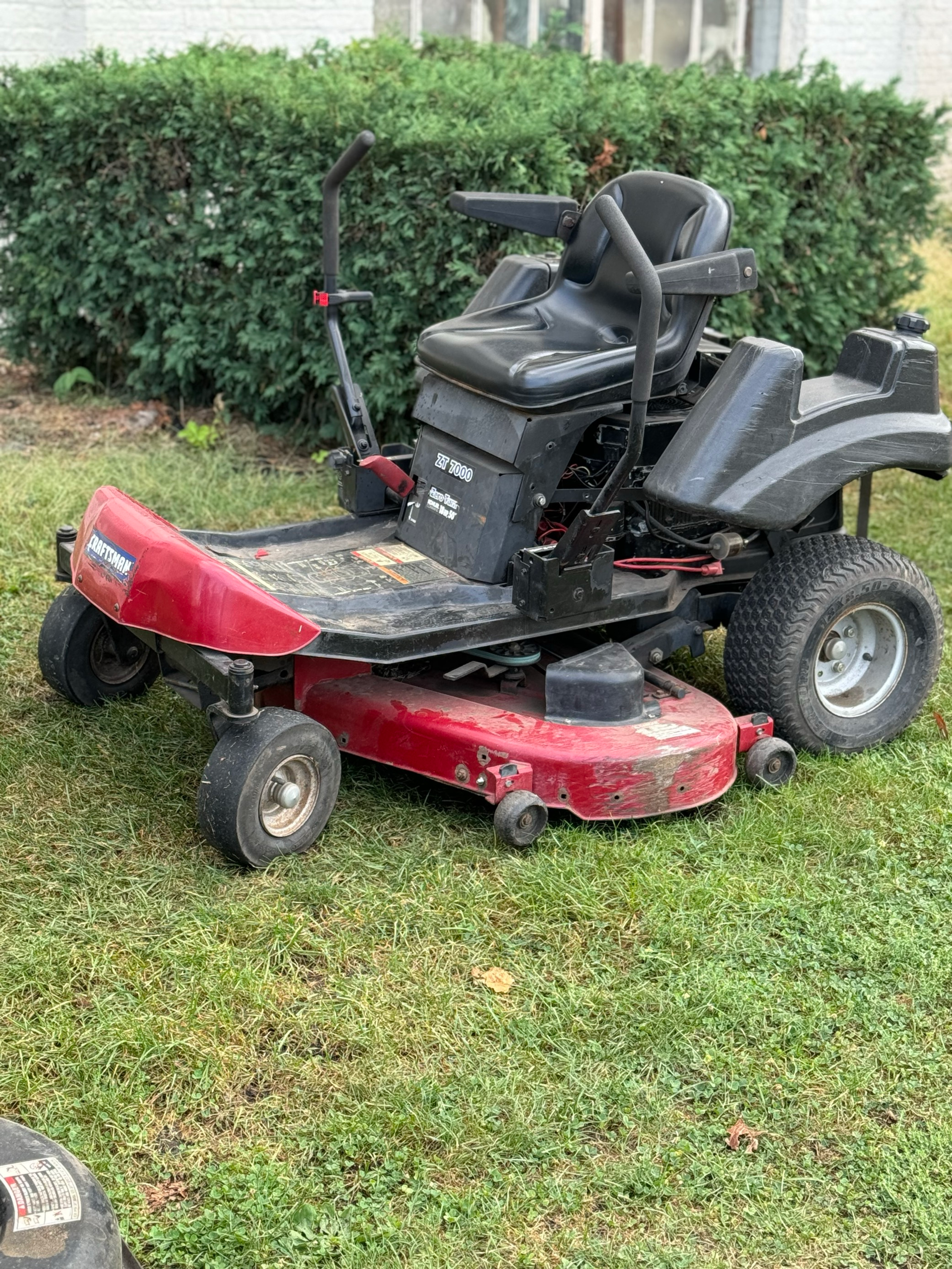 A row of red lawn mowers are parked in a grassy yard.