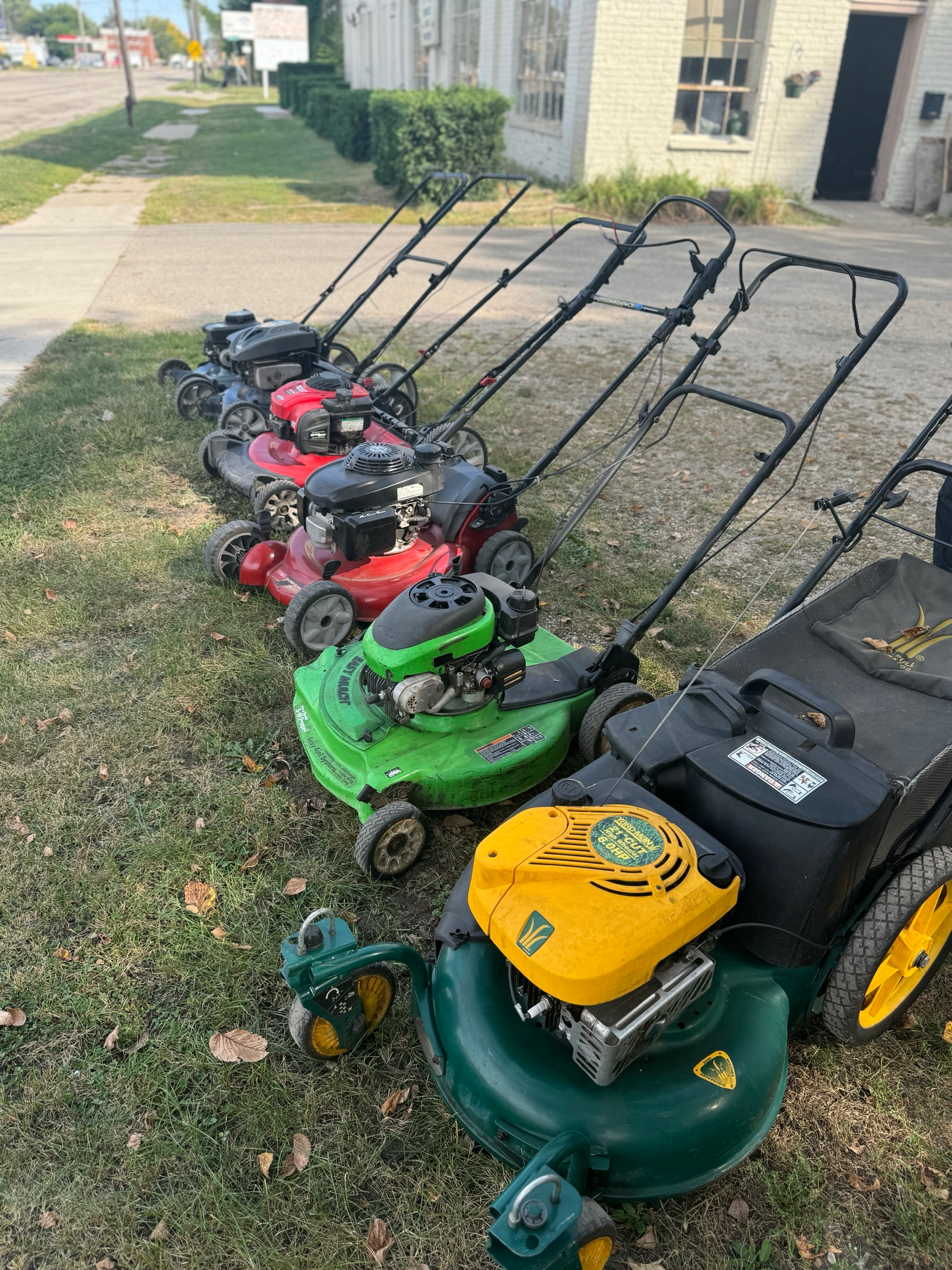 A red tractor is parked in the grass next to a lawn mower.