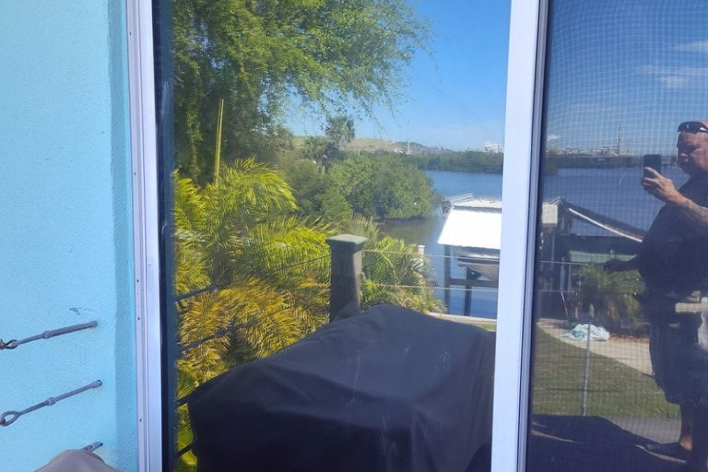 Patio view through a glass door, with a black grill, blue wall, trees, and water in the distance