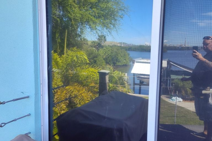 Patio view through a glass door, with a black grill, blue wall, trees, and water in the distance