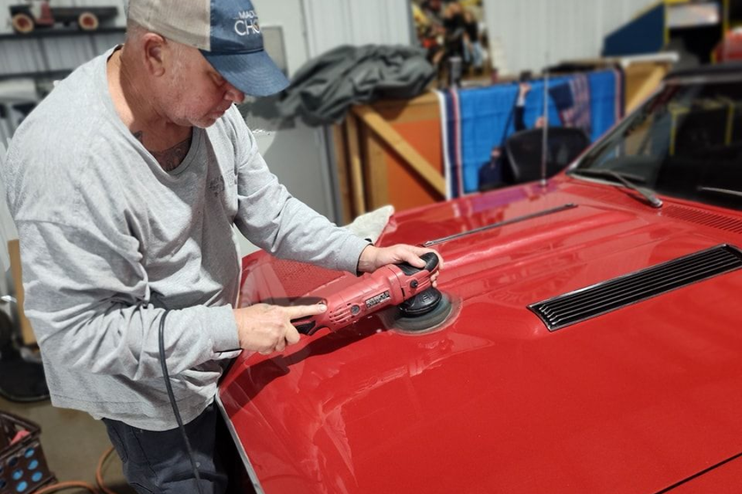 Person polishing a red car hood in a garage