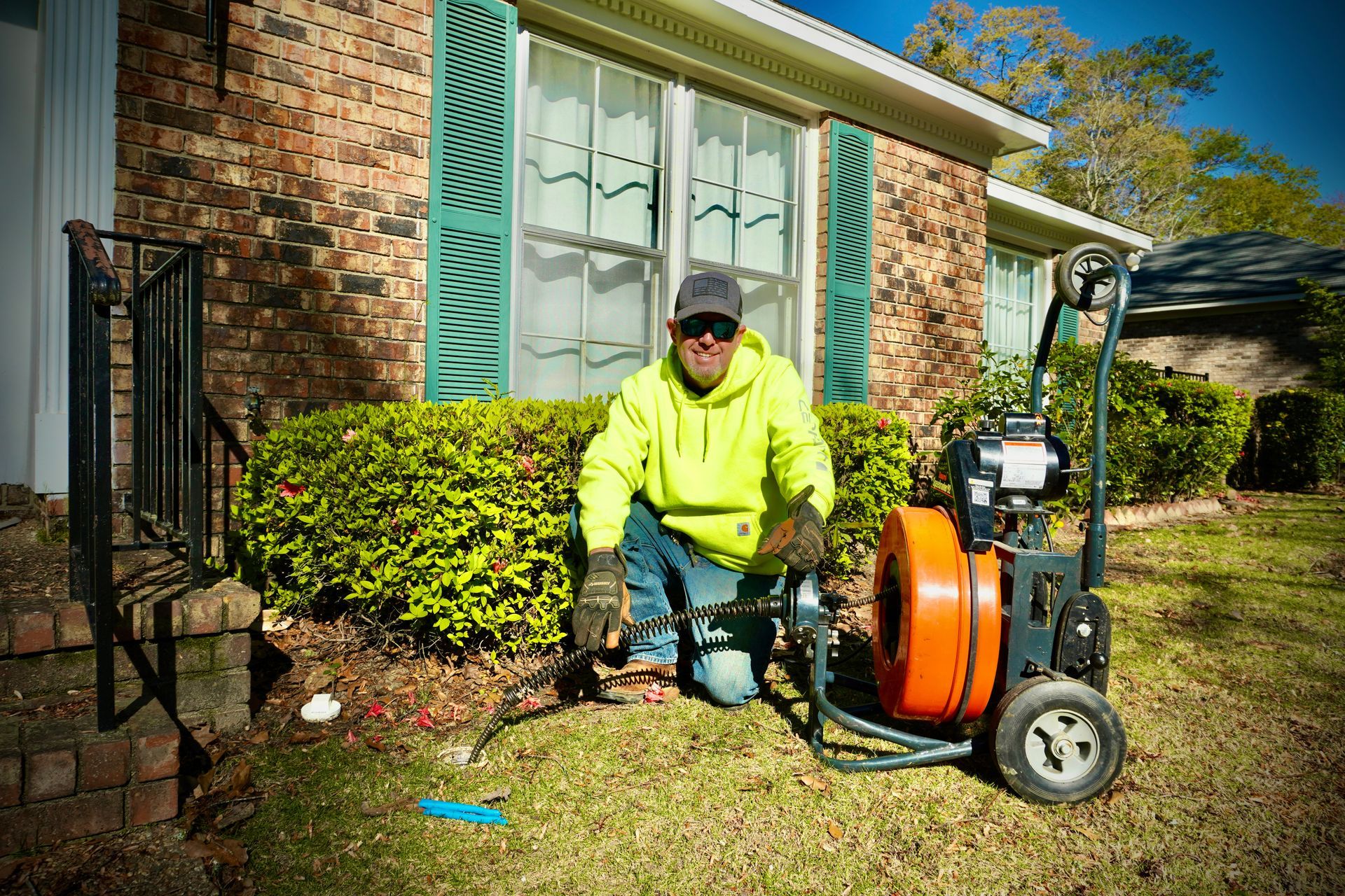 Plumber kneeling by an orange drain cleaning machine, clearing a residential sewer line.