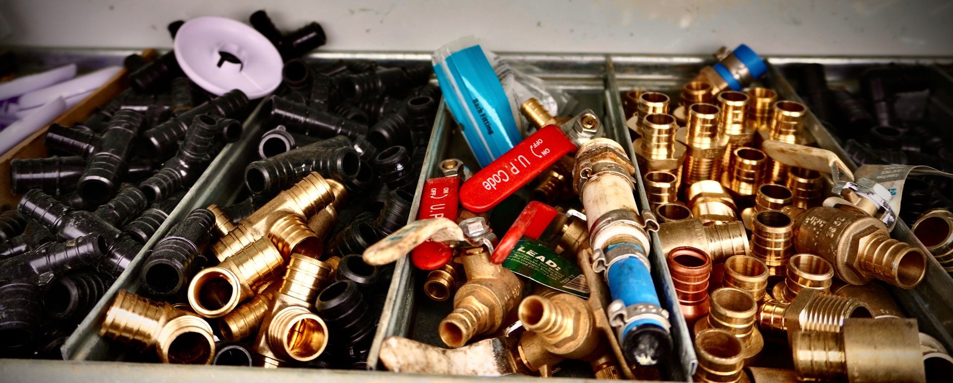 Various plumbing fittings in a tray, including brass, black, and red valves.