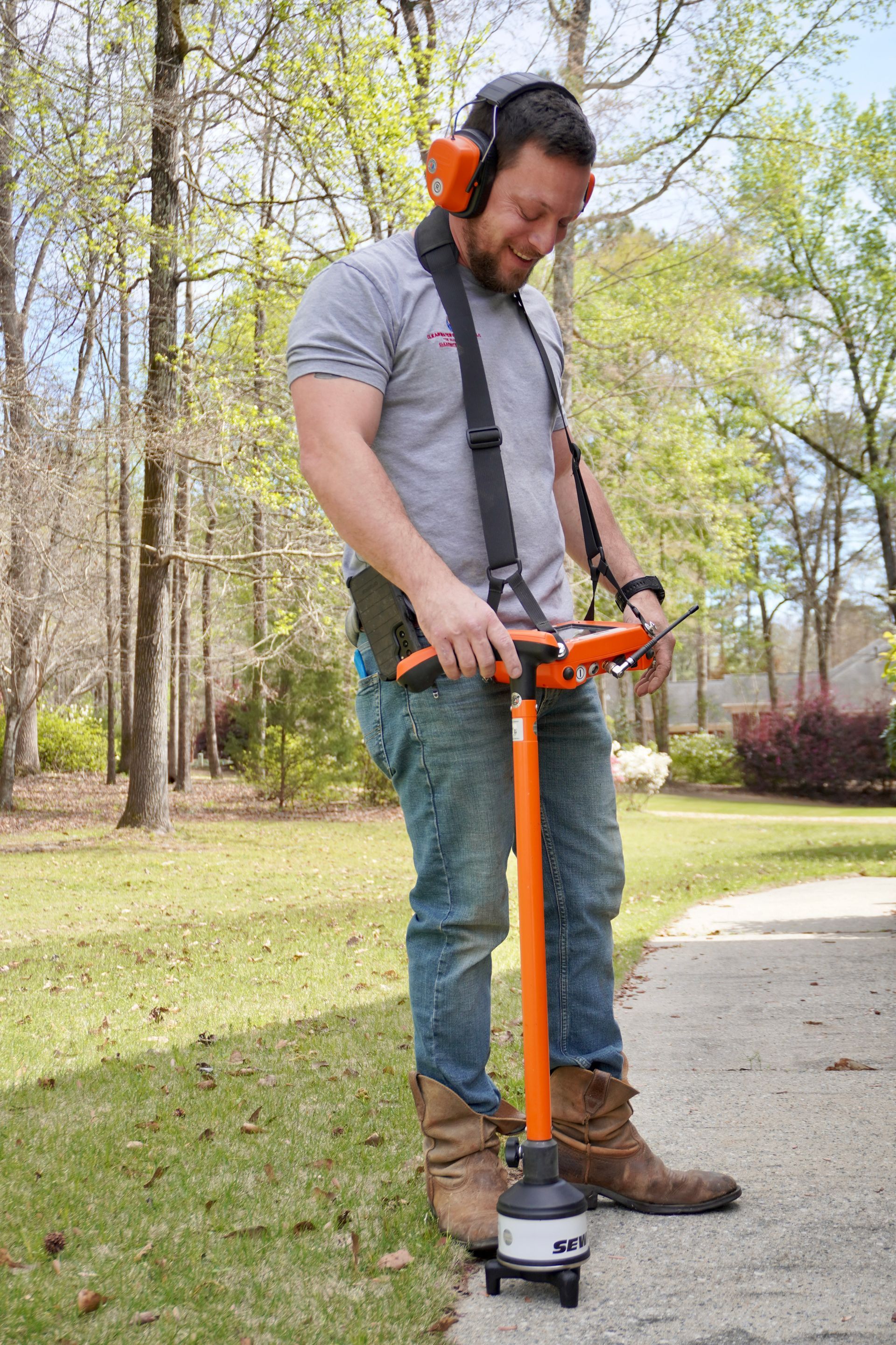 Man using utility locator in yard. Orange tool, ear protection. Sunny day.