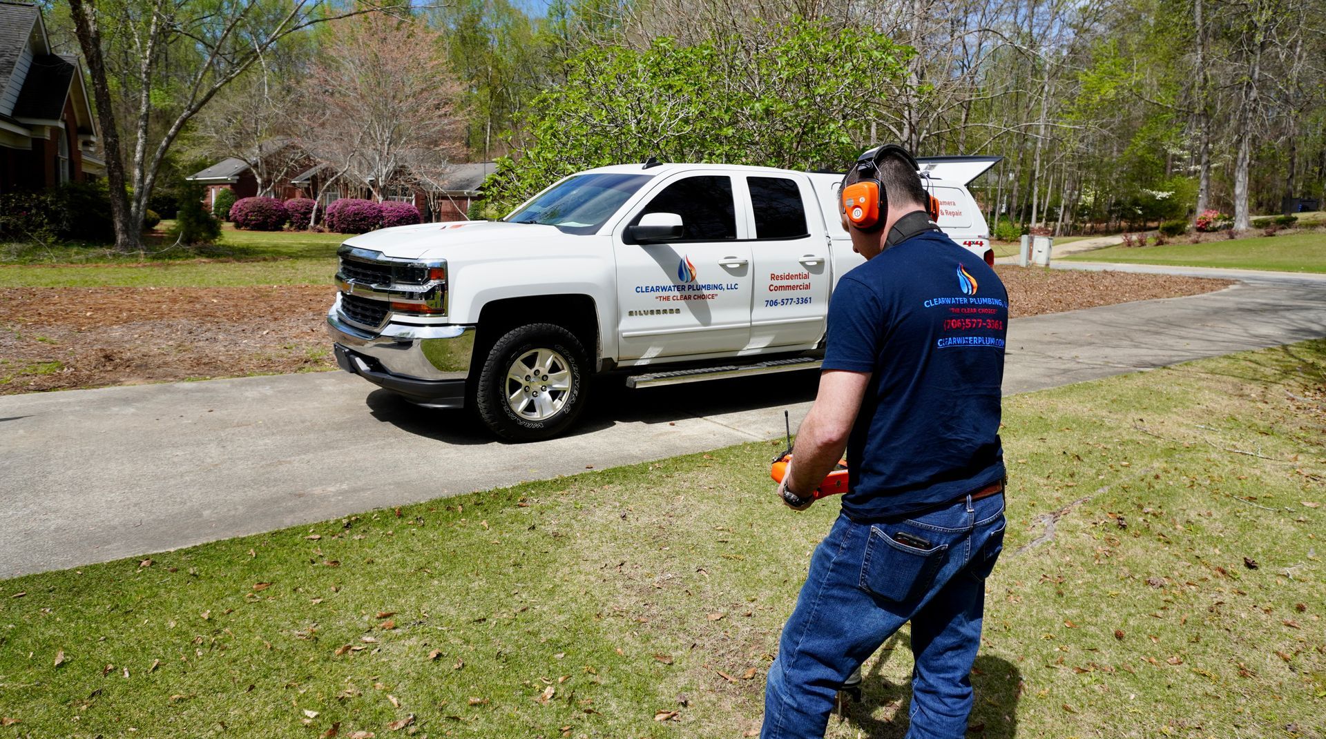 Man with remote, near a white truck on a driveway, in a grassy area.