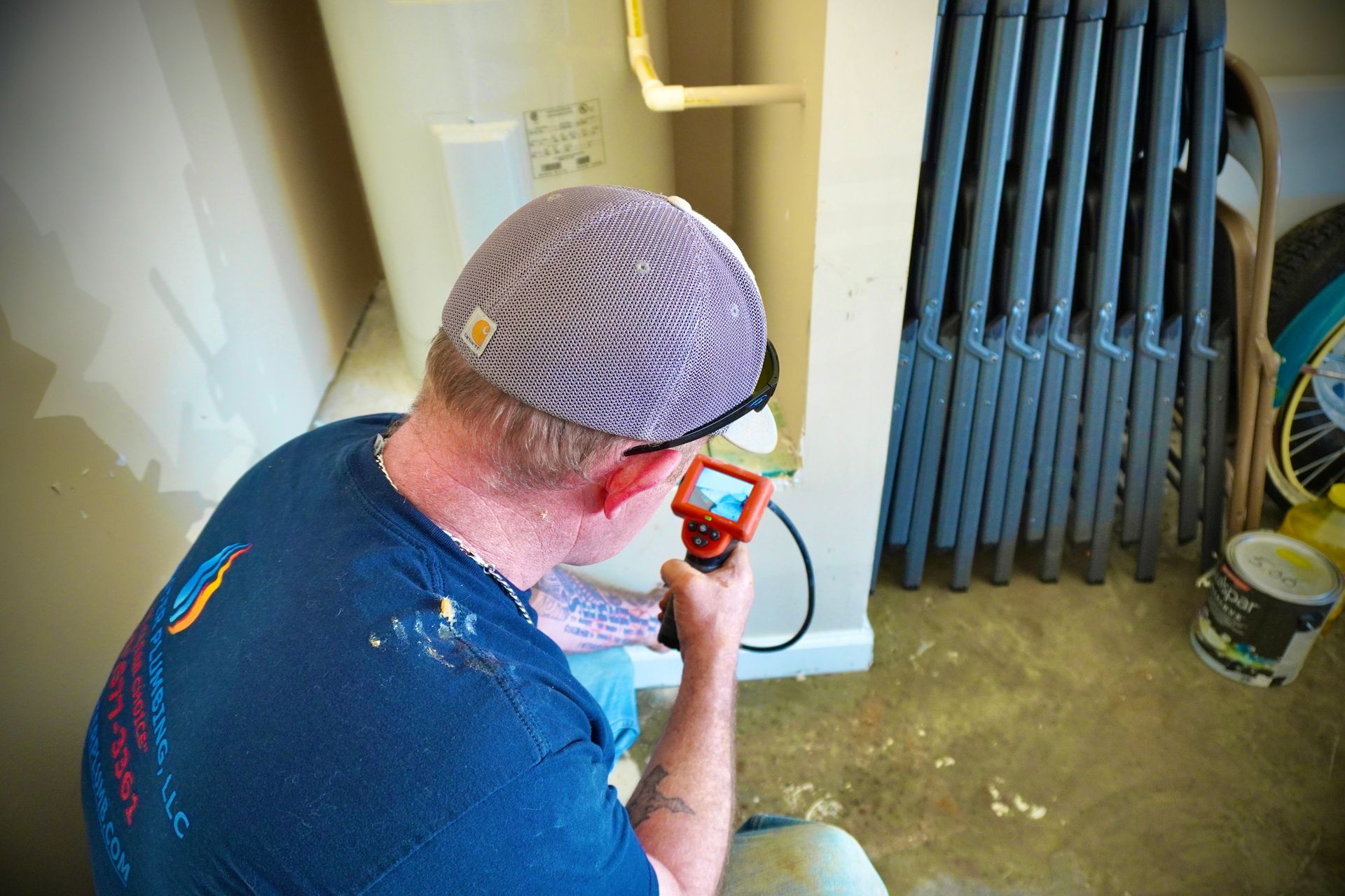 Man inspecting electrical outlet with a device, wearing a hat and safety glasses.