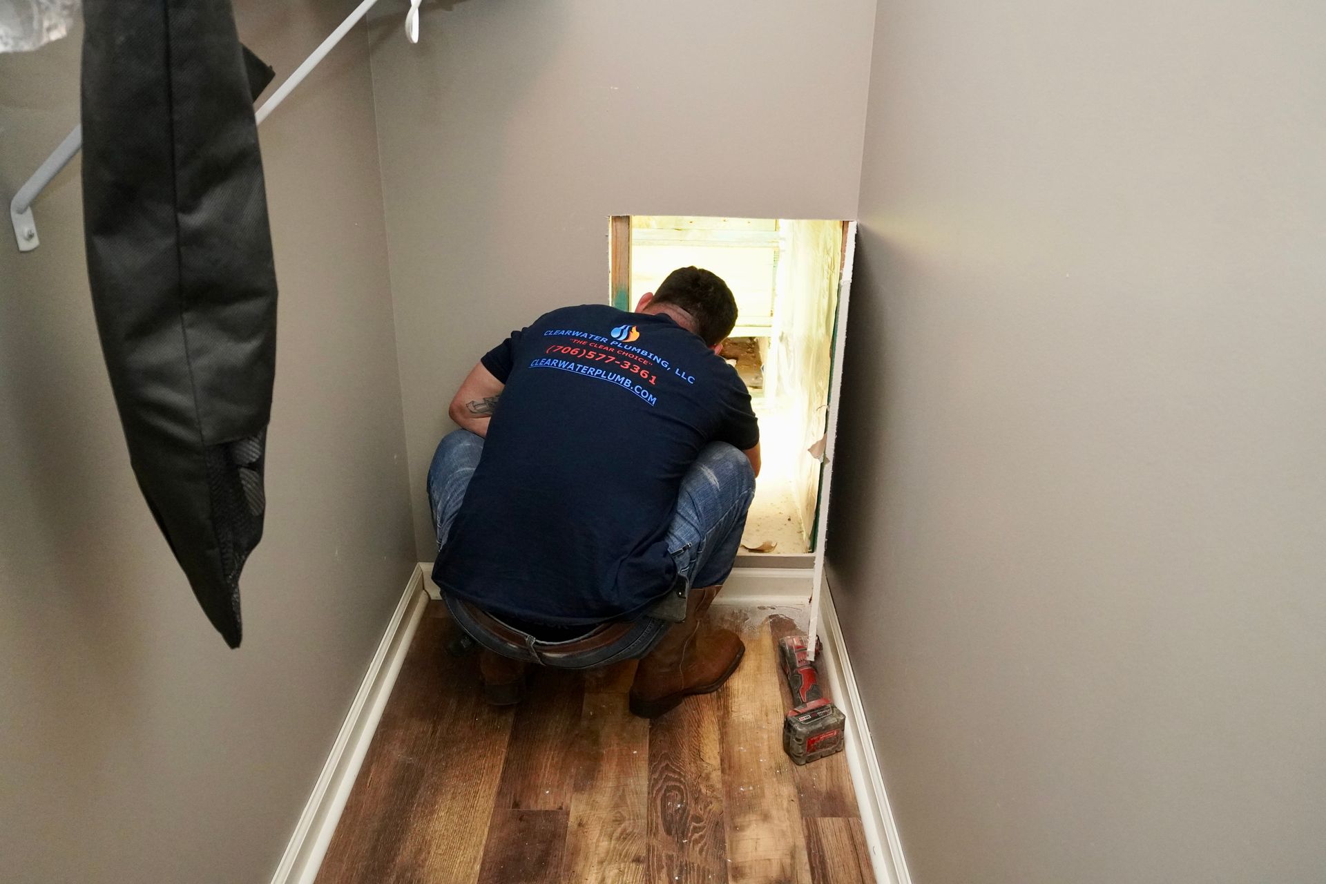 Man crouches in a narrow space, entering a crawl space. Room has wood-look floors, tan walls.