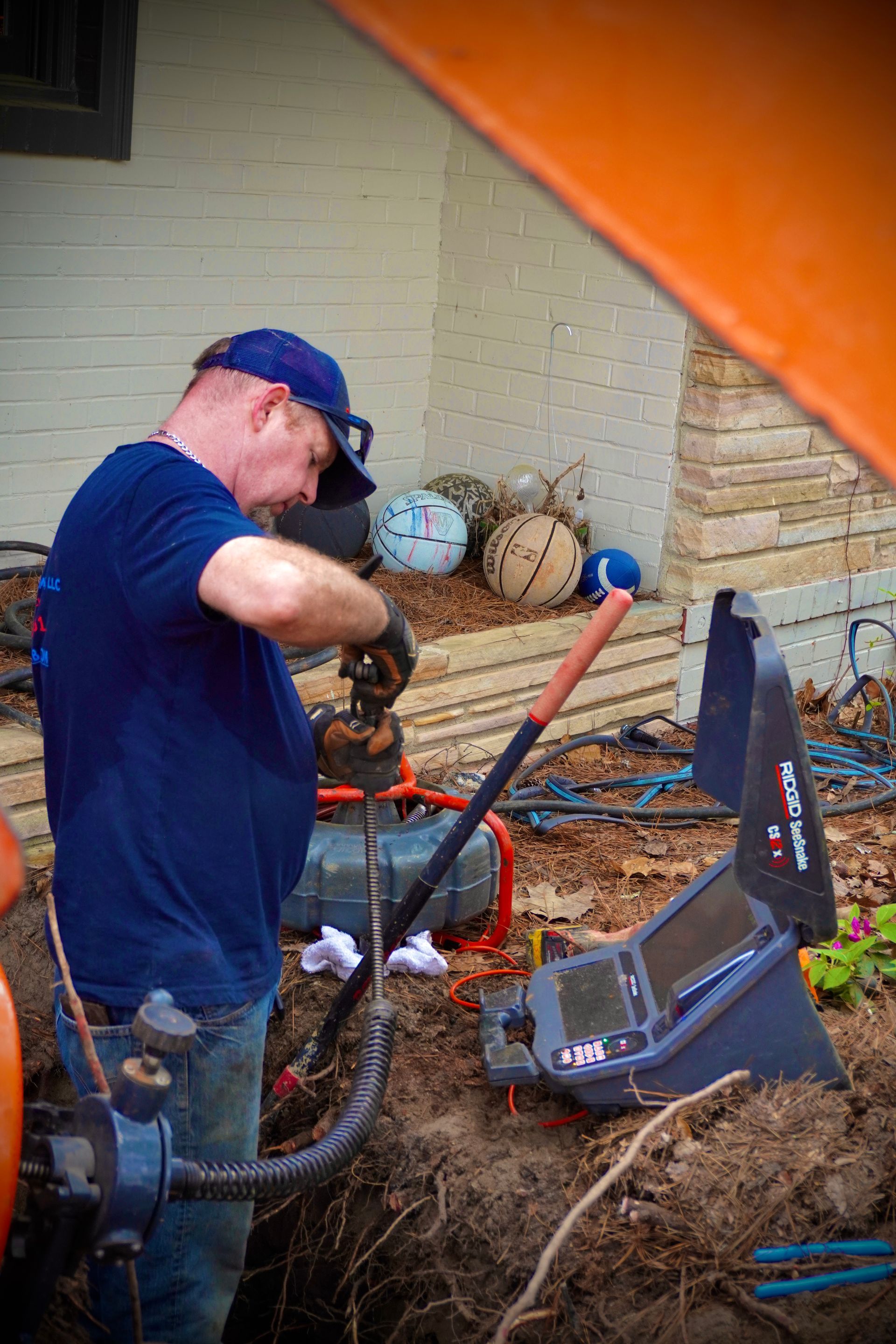 Plumber inspecting pipes with a video camera in a trench near a house.