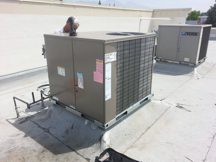 HVAC units on a rooftop. A technician works on the center unit on a sunny day.