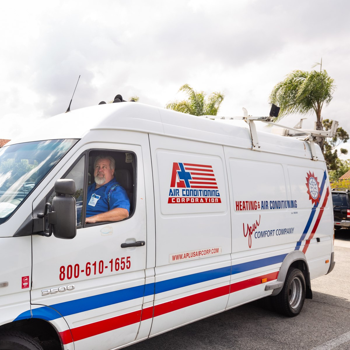 Woman in straw hat smiles, holding wine glass near a lake.