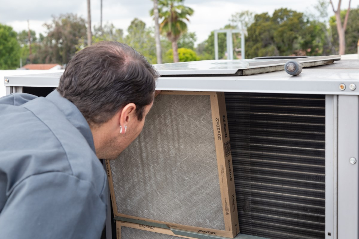 Woman in straw hat smiles, holding wine glass near a lake.